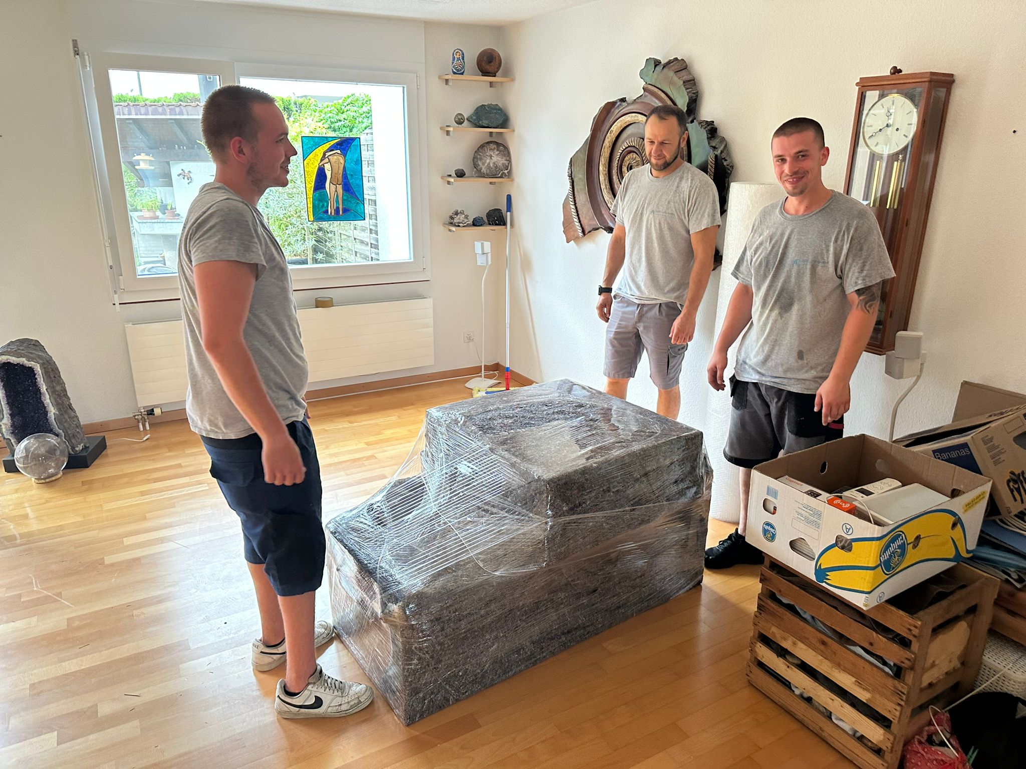 Drei Mitarbeitende mit sorgfältig in Schutzfolie verpackten Möbeln in einer Wohnung