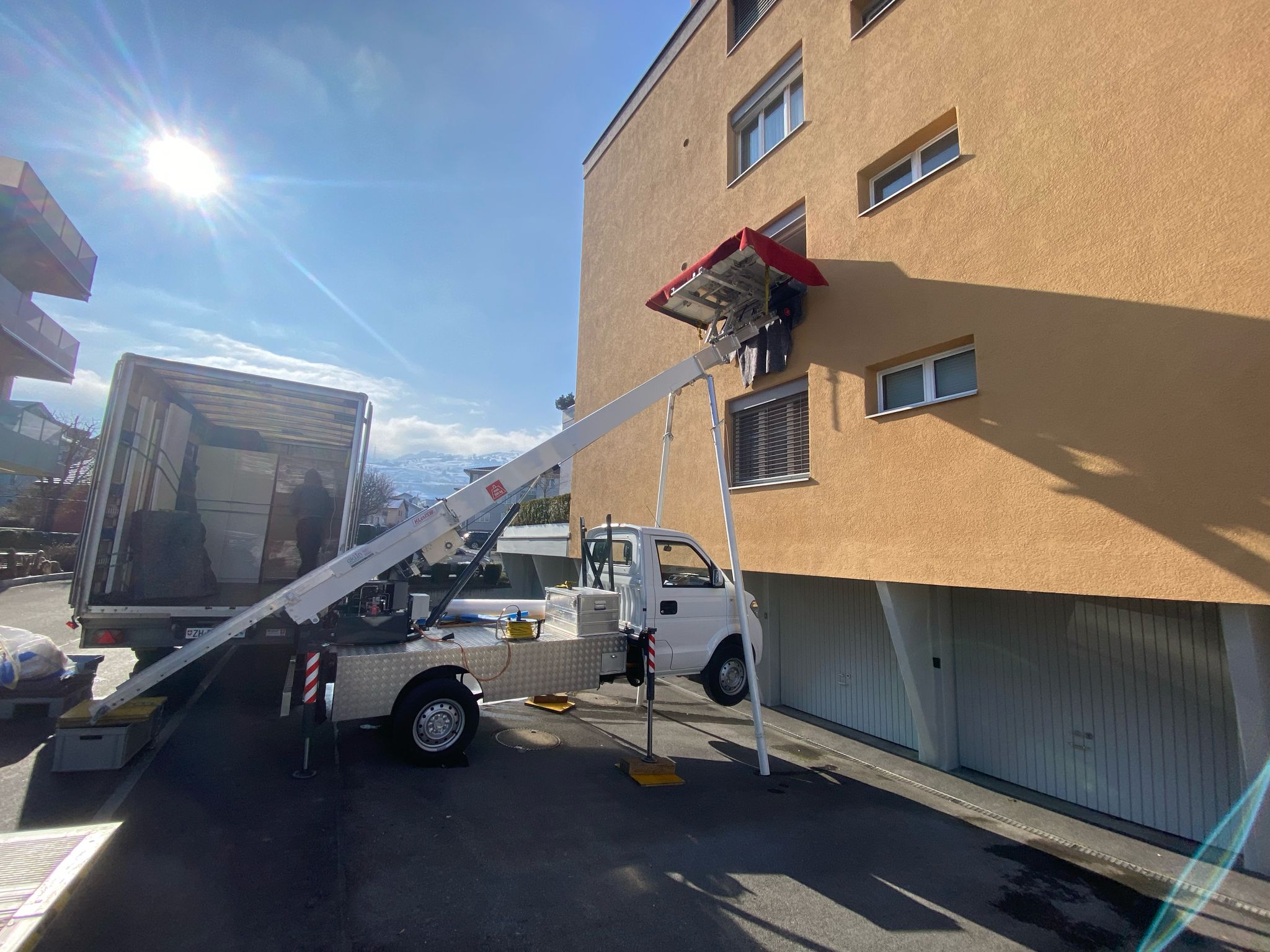 Lieferwagen mit Aussenlift an einem Haus, im Hintergrund Berge